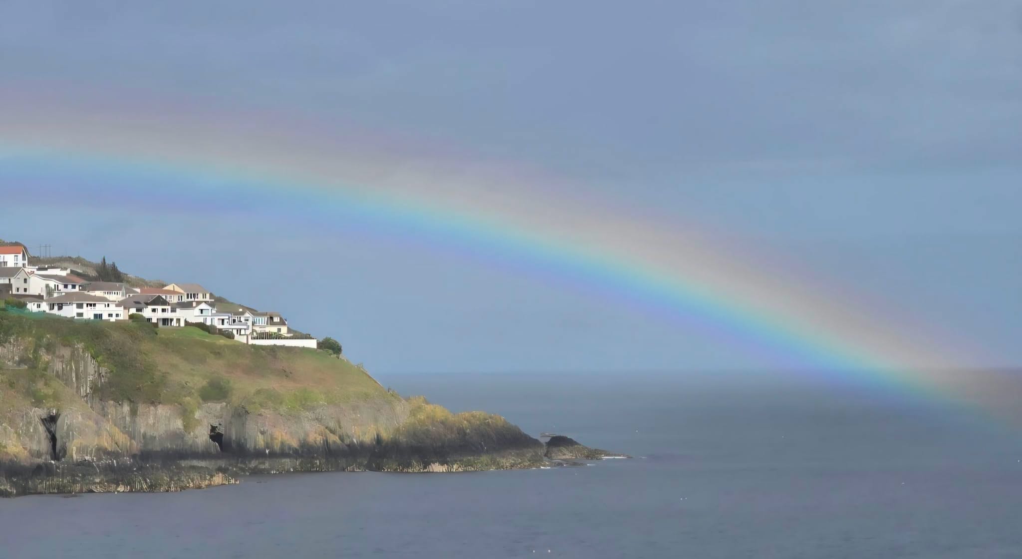 A rainbow arcing over the sea at Onchan Head, with clifftop houses